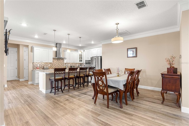 dining space with light wood-type flooring, a textured ceiling, and ornamental molding