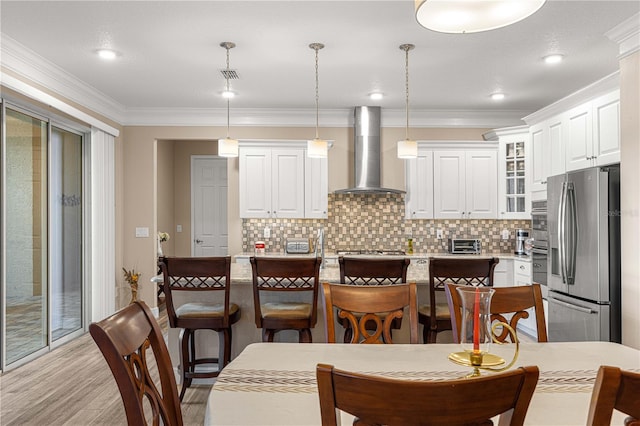 kitchen with decorative light fixtures, stainless steel refrigerator with ice dispenser, an island with sink, white cabinets, and wall chimney exhaust hood