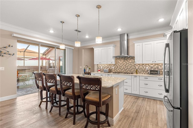 kitchen featuring white cabinetry, appliances with stainless steel finishes, wall chimney exhaust hood, and a center island with sink