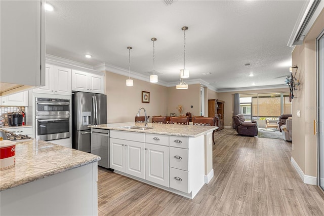 kitchen featuring white cabinets, hanging light fixtures, sink, an island with sink, and light hardwood / wood-style flooring