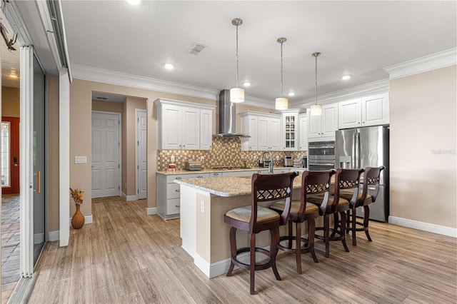 kitchen with stainless steel appliances, a center island with sink, wall chimney exhaust hood, white cabinetry, and light hardwood / wood-style flooring