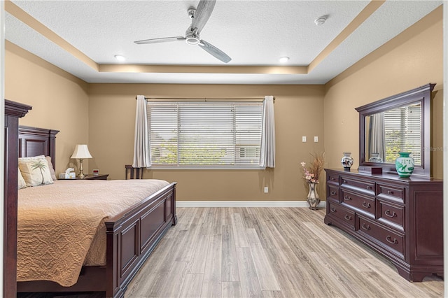 bedroom with ceiling fan, a textured ceiling, light hardwood / wood-style floors, and a raised ceiling