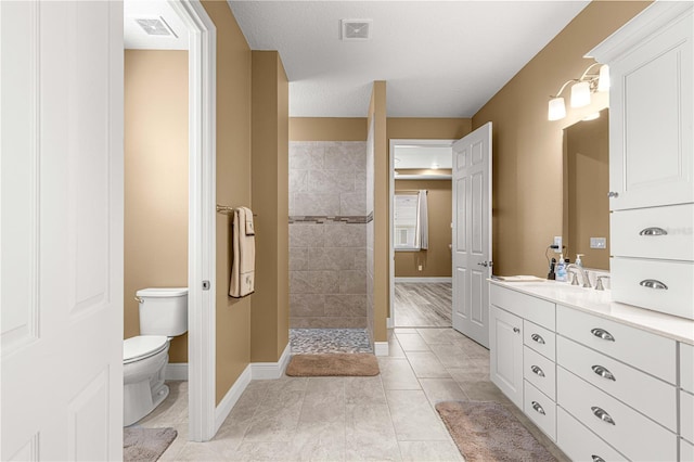 bathroom featuring a tile shower, vanity, a textured ceiling, tile patterned flooring, and toilet