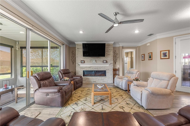 living room featuring ornamental molding, ceiling fan, a large fireplace, and plenty of natural light