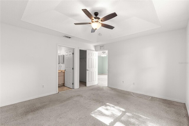 unfurnished bedroom featuring ceiling fan, connected bathroom, light carpet, and a tray ceiling