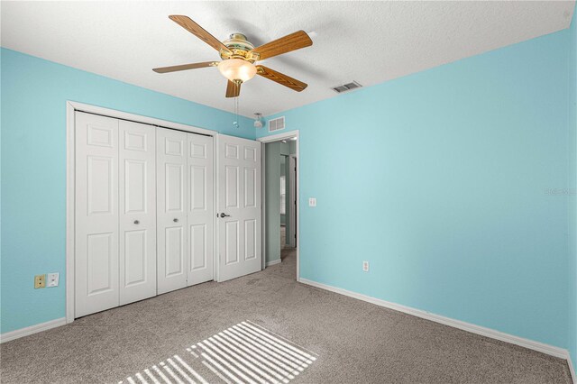 unfurnished bedroom with ceiling fan, a textured ceiling, a closet, and light colored carpet