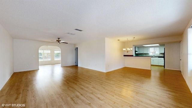 unfurnished living room featuring ceiling fan with notable chandelier, light wood-type flooring, and a textured ceiling