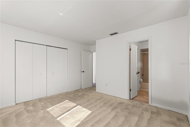 unfurnished bedroom with a closet, a textured ceiling, light carpet, and ensuite bathroom