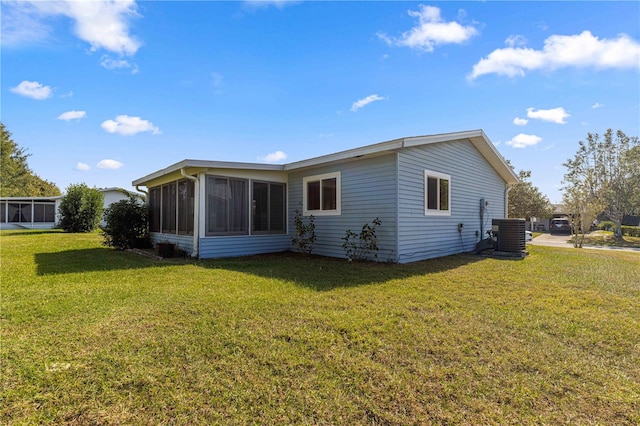 rear view of house featuring central AC, a sunroom, and a lawn