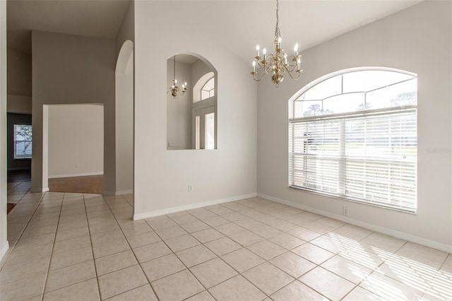 tiled spare room featuring plenty of natural light, lofted ceiling, and a notable chandelier