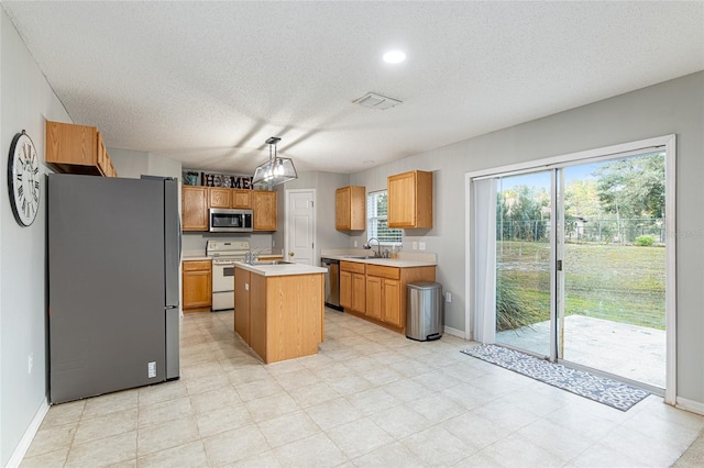 kitchen with a textured ceiling, stainless steel appliances, sink, decorative light fixtures, and a kitchen island