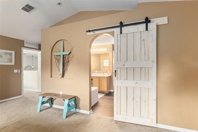 hallway with light carpet, a textured ceiling, vaulted ceiling, sink, and a barn door