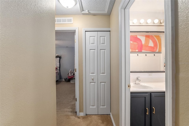 hall featuring a textured ceiling, light colored carpet, and sink