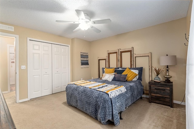 bedroom with a textured ceiling, light colored carpet, a closet, and ceiling fan