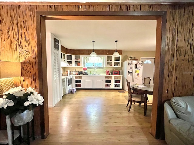 kitchen featuring sink, light hardwood / wood-style flooring, white refrigerator with ice dispenser, pendant lighting, and wooden walls