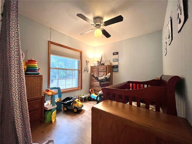 bedroom featuring hardwood / wood-style flooring, a nursery area, and ceiling fan