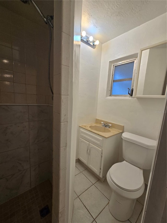 bathroom with a textured ceiling, toilet, vanity, and tiled shower