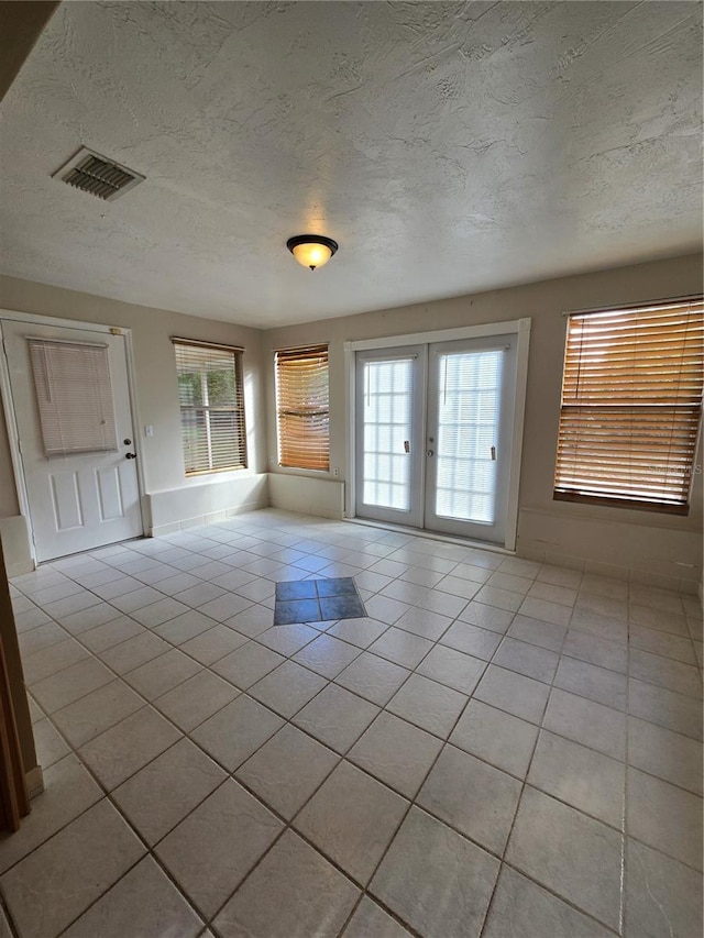 spare room featuring light tile patterned flooring, french doors, and a textured ceiling