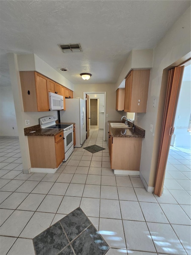 kitchen featuring white appliances, sink, light tile patterned flooring, and a textured ceiling