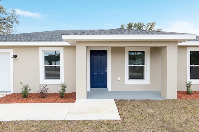 entrance to property featuring stucco siding, covered porch, and roof with shingles