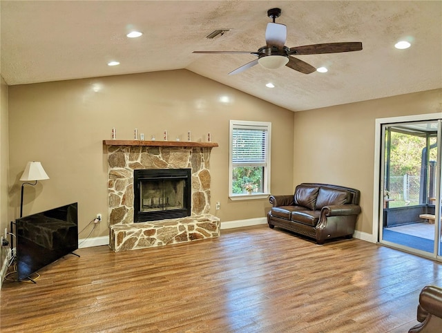 living area with ceiling fan, a stone fireplace, a textured ceiling, vaulted ceiling, and hardwood / wood-style flooring