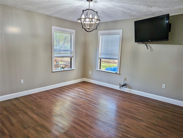 spare room featuring a textured ceiling, dark hardwood / wood-style flooring, an inviting chandelier, and a wealth of natural light