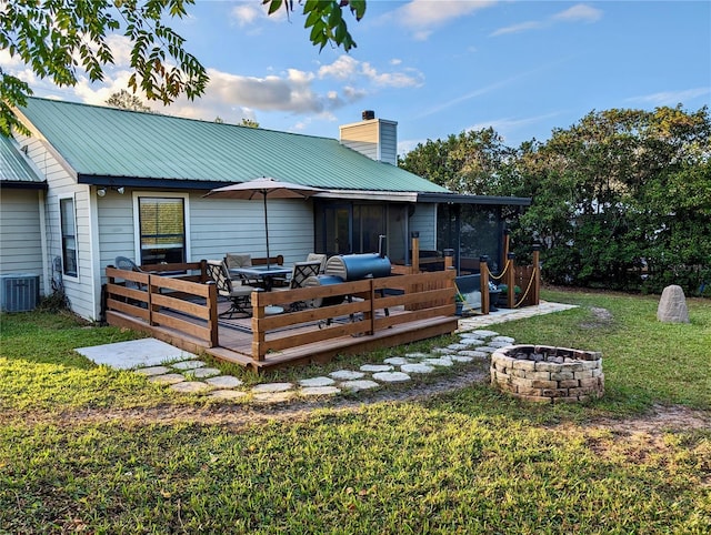 rear view of house with a sunroom, a lawn, cooling unit, a wooden deck, and an outdoor fire pit