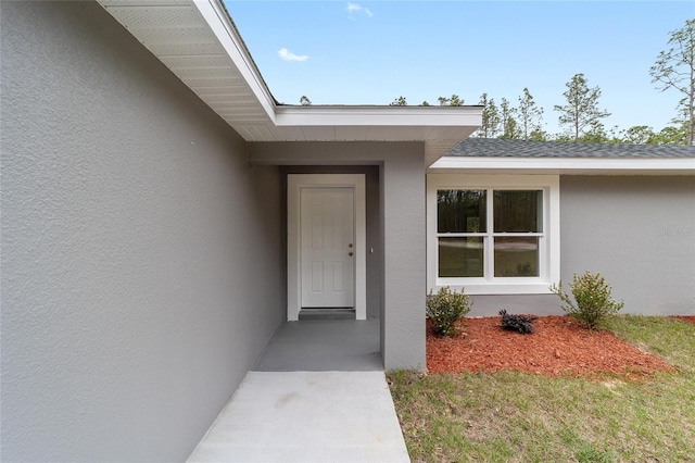 entrance to property with roof with shingles and stucco siding