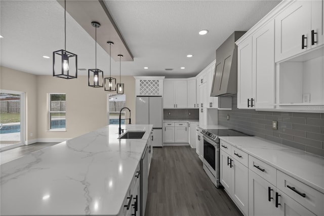 kitchen featuring pendant lighting, white cabinetry, sink, stainless steel appliances, and wall chimney range hood