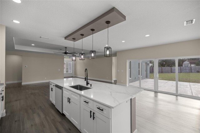 kitchen featuring dishwasher, sink, white cabinets, a kitchen island with sink, and light stone countertops