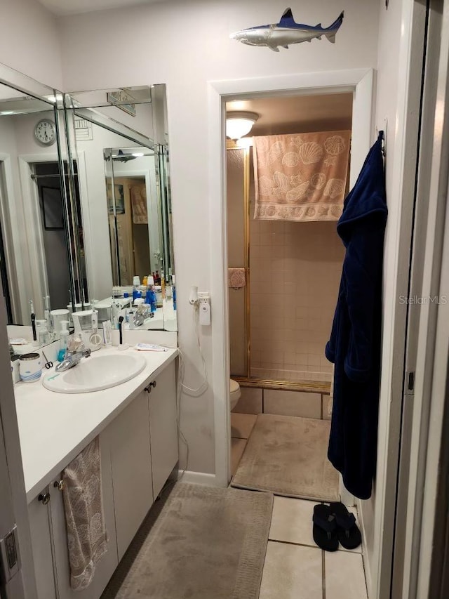 bathroom with a tile shower, tile patterned flooring, vanity, and toilet