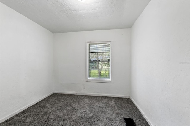 empty room with dark carpet and a textured ceiling