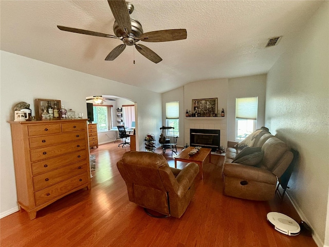 living room with a textured ceiling, ceiling fan, a tile fireplace, hardwood / wood-style flooring, and lofted ceiling