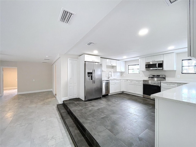 kitchen featuring white cabinets, appliances with stainless steel finishes, light stone countertops, and sink