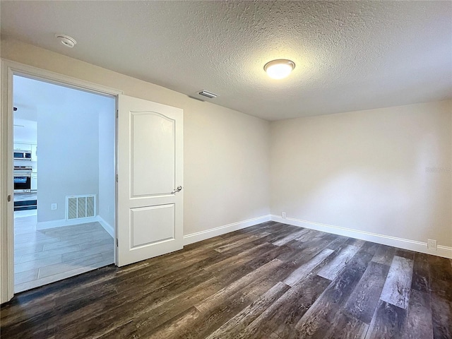 spare room with a textured ceiling and dark hardwood / wood-style flooring