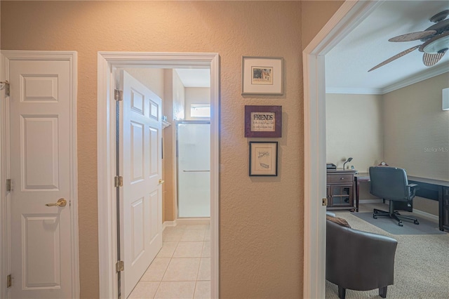 corridor featuring light tile patterned floors, a textured wall, ornamental molding, and baseboards