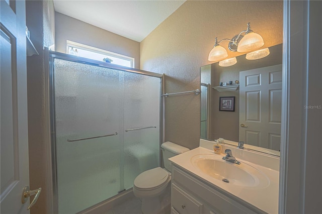 bathroom with a textured wall, a shower stall, toilet, and vanity