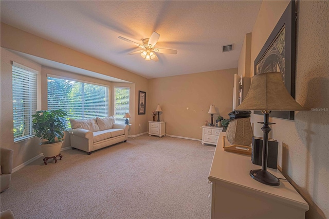 living area with ceiling fan, a textured ceiling, light carpet, visible vents, and baseboards