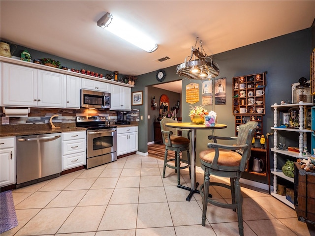 kitchen with hanging light fixtures, appliances with stainless steel finishes, tasteful backsplash, light tile patterned flooring, and white cabinetry