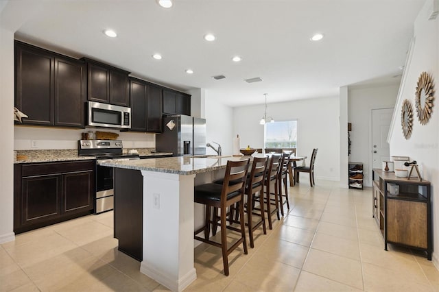 kitchen with a kitchen bar, a center island with sink, hanging light fixtures, light stone counters, and stainless steel appliances