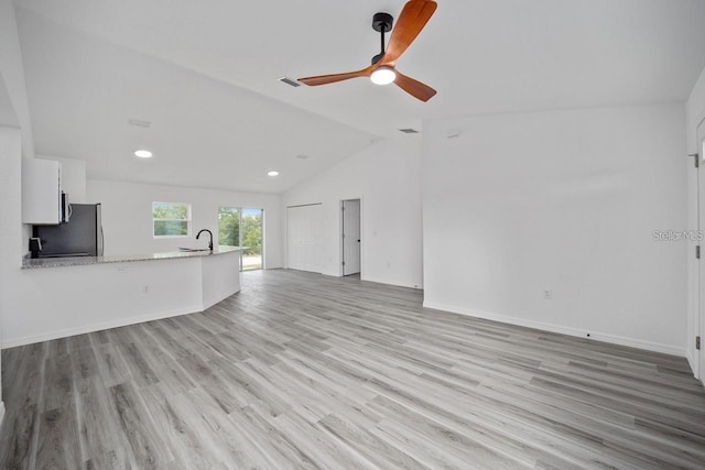 unfurnished living room with ceiling fan, sink, light hardwood / wood-style flooring, and vaulted ceiling