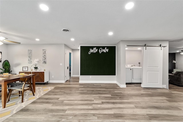 interior space featuring a barn door, light hardwood / wood-style floors, washer and clothes dryer, and ceiling fan