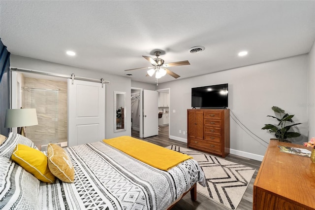 bedroom with wood-type flooring, a barn door, a textured ceiling, and ceiling fan