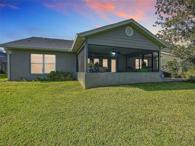 back house at dusk with a yard and a sunroom