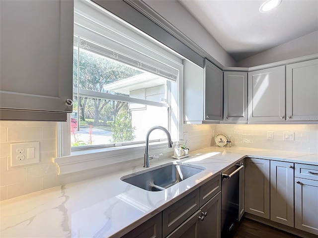 kitchen with gray cabinetry, dishwasher, sink, tasteful backsplash, and light stone counters