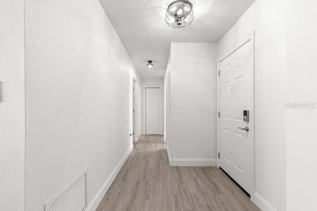 hall with a textured ceiling and light hardwood / wood-style flooring