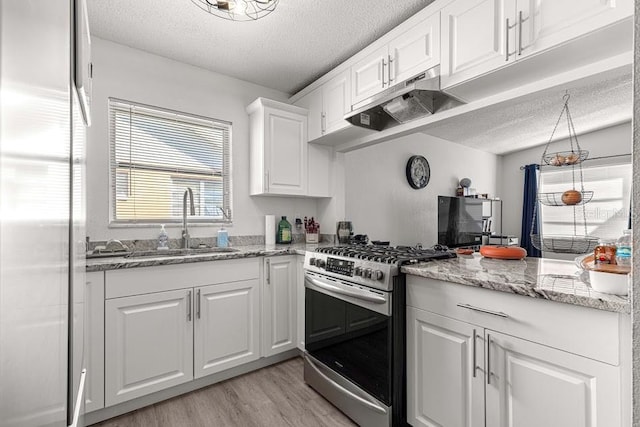 kitchen with gas range, white cabinetry, sink, light hardwood / wood-style floors, and a textured ceiling