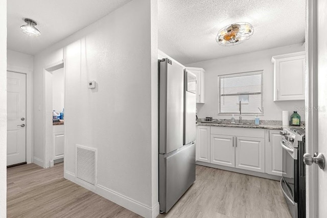 kitchen featuring sink, stainless steel appliances, light hardwood / wood-style floors, a textured ceiling, and white cabinets