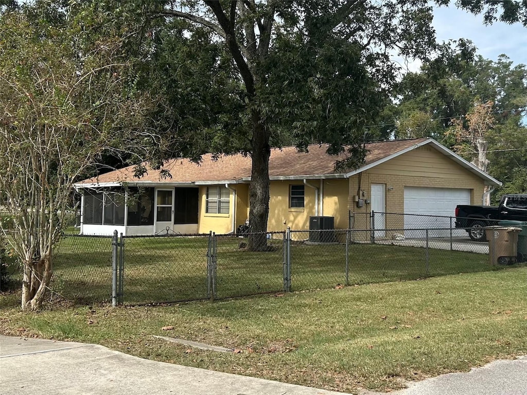 view of front of home featuring a front yard, a garage, central AC unit, and a sunroom