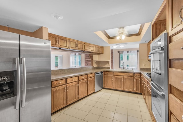 kitchen with sink, a raised ceiling, kitchen peninsula, light tile patterned flooring, and appliances with stainless steel finishes